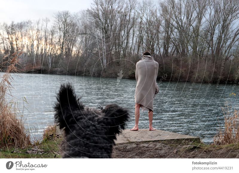 naked young man stands, wrapped in a blanket, by a wintry lake and is watched by a dog Man Dog Cold challenge Winter Ice bathing Freeze Motive sanity mental