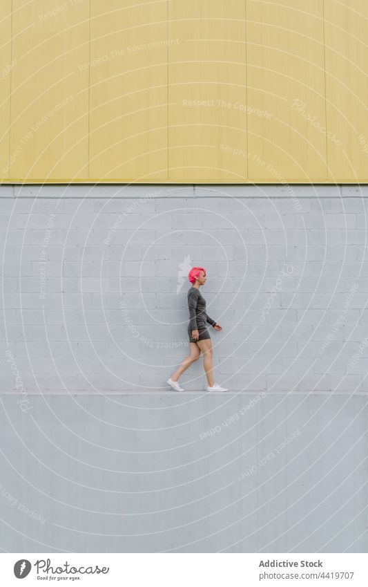 Young man in sportswear walking near wall woman trendy street urban confident exterior building facade modern gray contemporary daytime outfit alone daylight