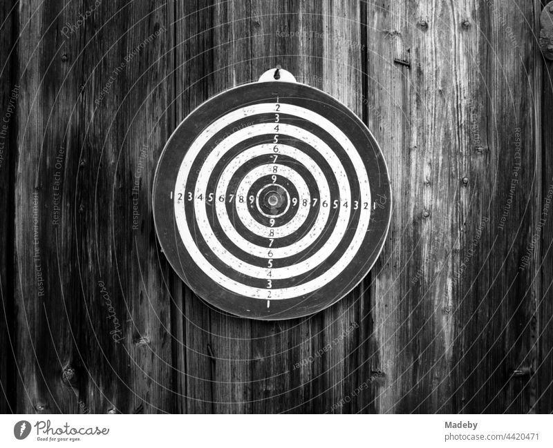 Circular old dartboard on a barn wall made of rustic wood on a farm in Rudersau near Rottenbuch in the district of Weiheim-Schongau in Upper Bavaria, photographed in classic black and white