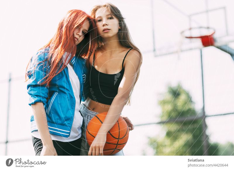 Portrait of two charming girls with a basketball on the sports field. Friendship, best friends, sports court holding friendship basketball court girlfriend