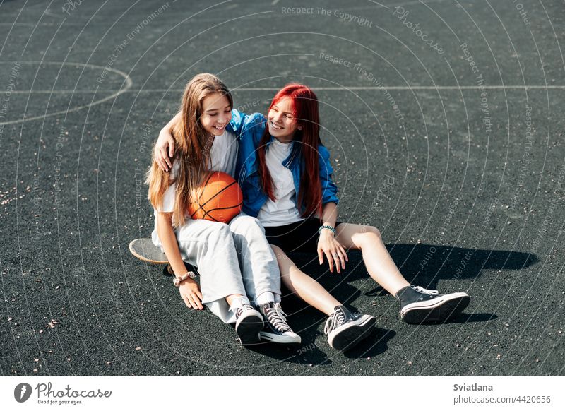 A couple of teenage girls on a sports street court with a basketball lifestyle relax after a game and talk. The concept of sports and a healthy lifestyle