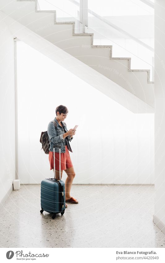 wide angle view of backpacker caucasian woman at train station using mobile phone app while waiting. Travel concept travel technology baggage internet online