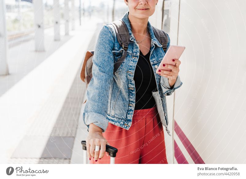 close up of backpacker caucasian woman holding luggage at train station ready to catch the train. Holding mobile phone while using app. Travel concept travel