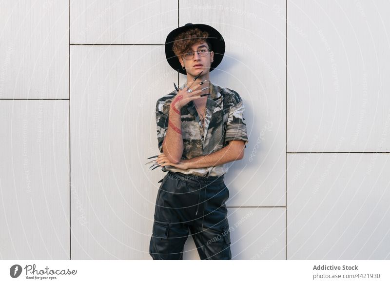Trendy model with hat against tiled wall fashion style individuality vain man trendy wear garment shirt ornament trousers street modern eyes closed