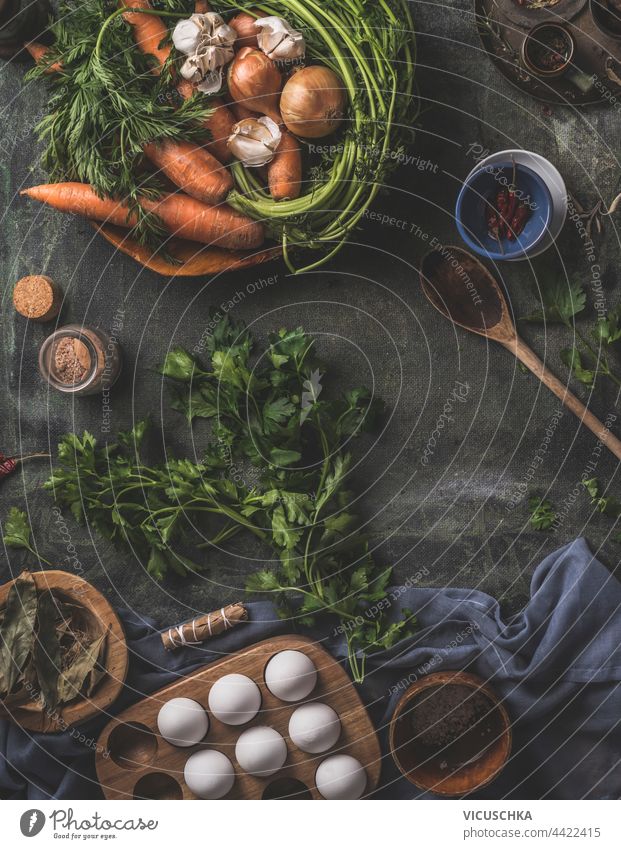 Healthy ingredients for tasty cooking at home. Fresh vegetables and herbs on a dark kitchen table with a wooden spoon, fresh eggs and dried seasonings . Top view