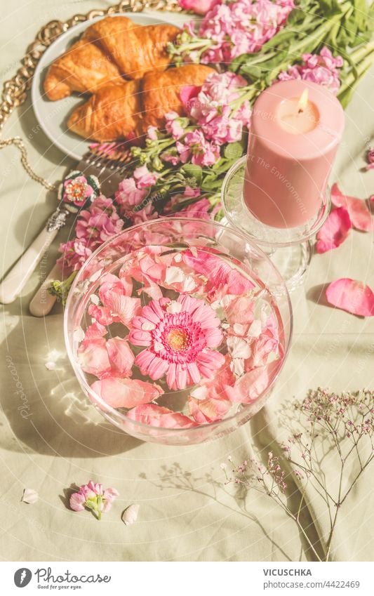 Glass water bowl with pink flowers on picnic blanket with Croissants and candles. Sunny day. Aesthetic picnic concept glass croissants sunny day