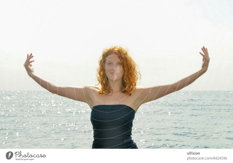 Happy happy portrait of a young elegant red-haired curly woman with outstretched arms by the sea at the beach in Italy with copy space, space for text Beach