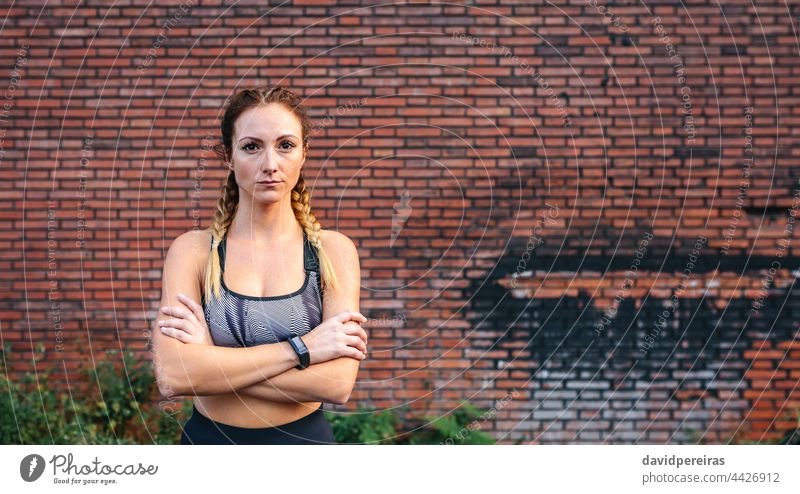 Sportswoman with crossed arms posing sportswoman brick wall looking camera copy space waist up empowerment active serious boxer braids adult background athletic