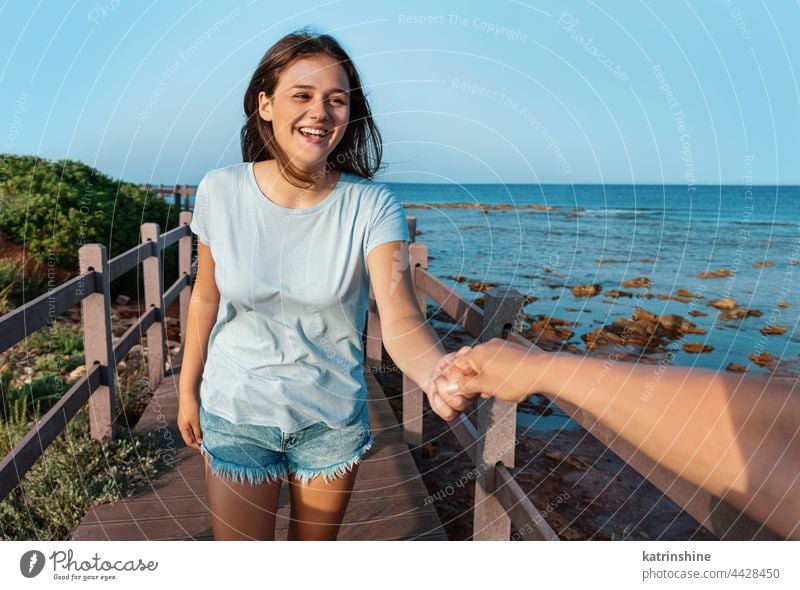 Happy teenage girls running on sidewalk by the sea at sunset young woman teenager hand mockup happy smiling t-shirt adolescent blue Caucasian walkside outdoor