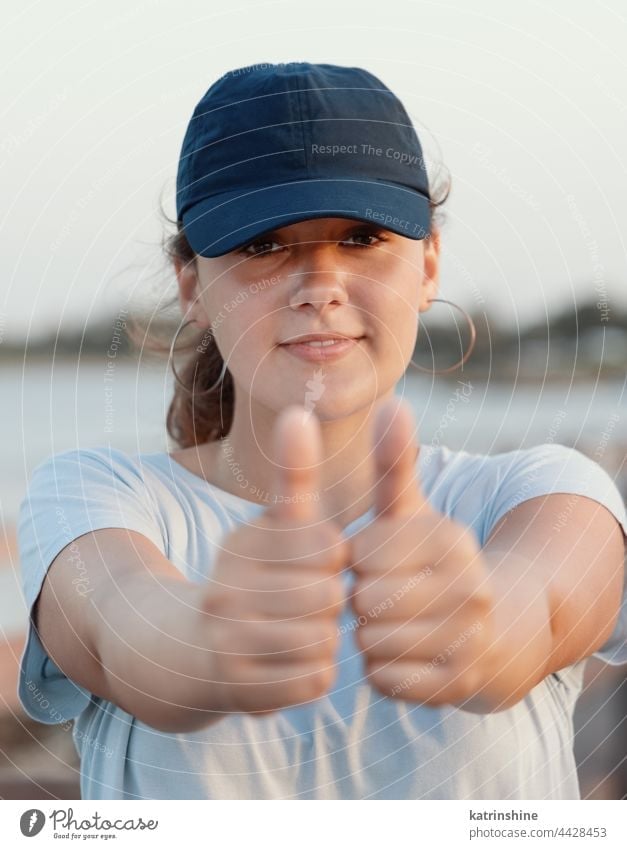 Teenage girl in blue baseball cap showing big thumbs up sunset teenager nature adolescent mockup smile head shot sea Caucasian outdoor vacation travel wearing
