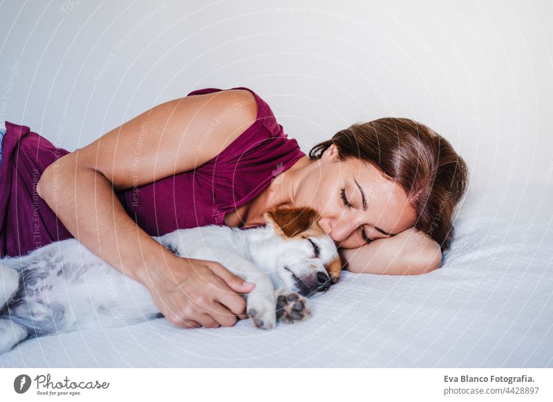 young caucasian woman at home resting on bed with cute jack russell dog. Pets, love and relax sleep kiss together togetherness 30s tired house sleeping owner