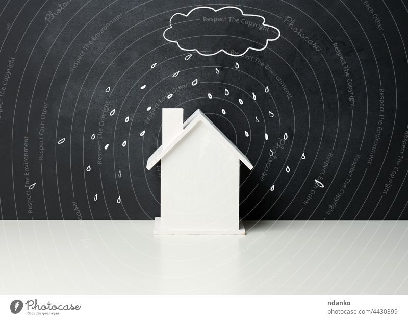 wooden house and a drawn cloud with rain with white chalk on a black chalk board. Real estate insurance concept problem storm family building small architecture