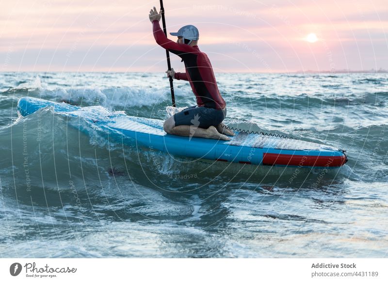 Man with paddle board in water to surfing man sup board surfer seashore wetsuit beach male surfboard sport hat ocean seaside water sports waterfront coastline