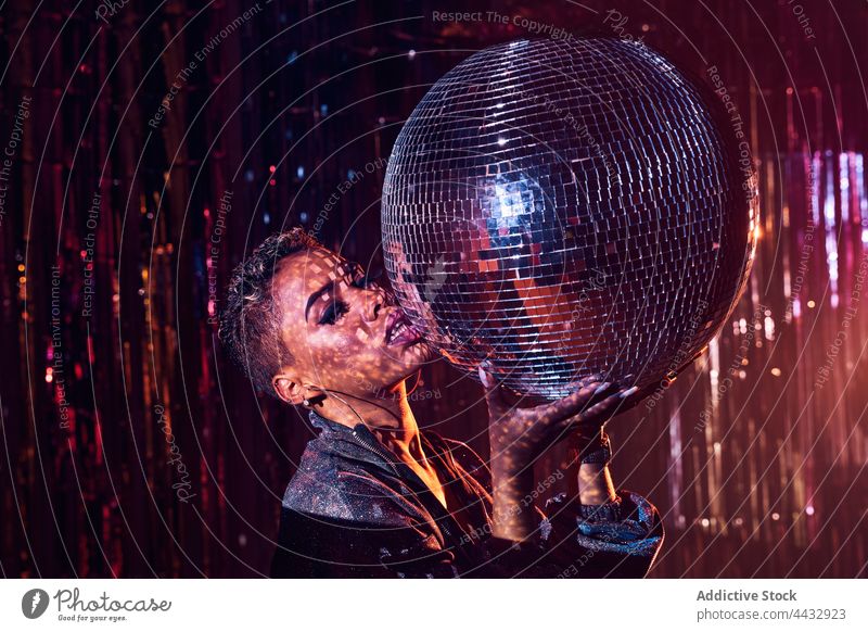 Stylish black model with makeup holding on disco ball touch lips individuality stylish gaze woman nightclub portrait tilt style cool haircut african american