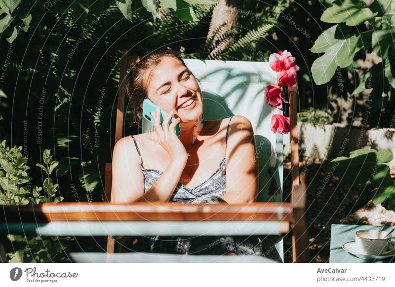 Woman laughing while making a phone call in a sunny garden during holidays, relax working from home communication connection mobile phone time technology