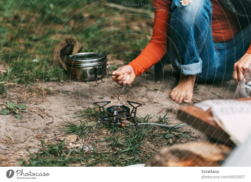 A woman cooks food with a portable gas burner in the forest female activity tourism camp outdoor nature adventure travel picnic hiking girl tourist trip