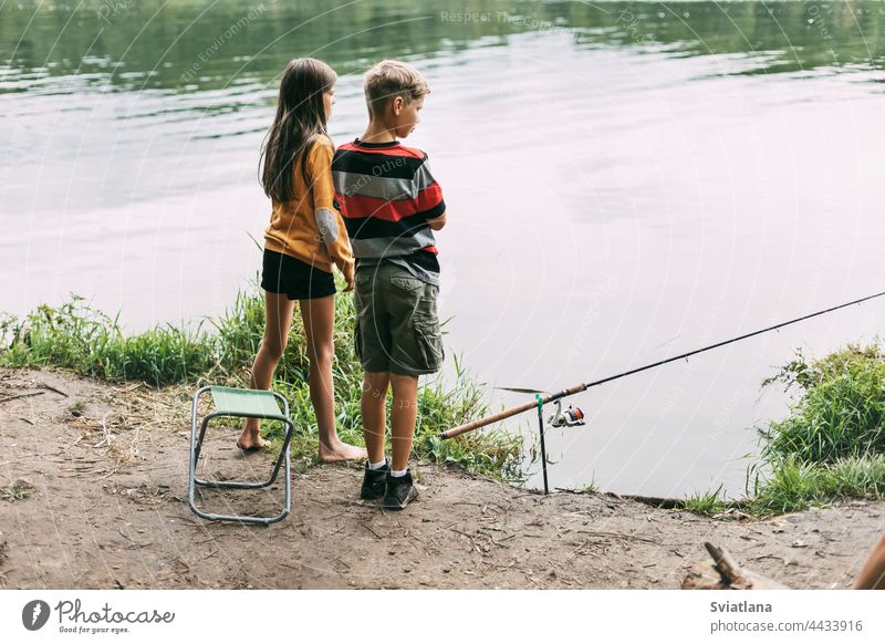 A brother and sister are standing on the river bank and fishing during a family vacation at a camping site. Time together, family vacation boy girl child