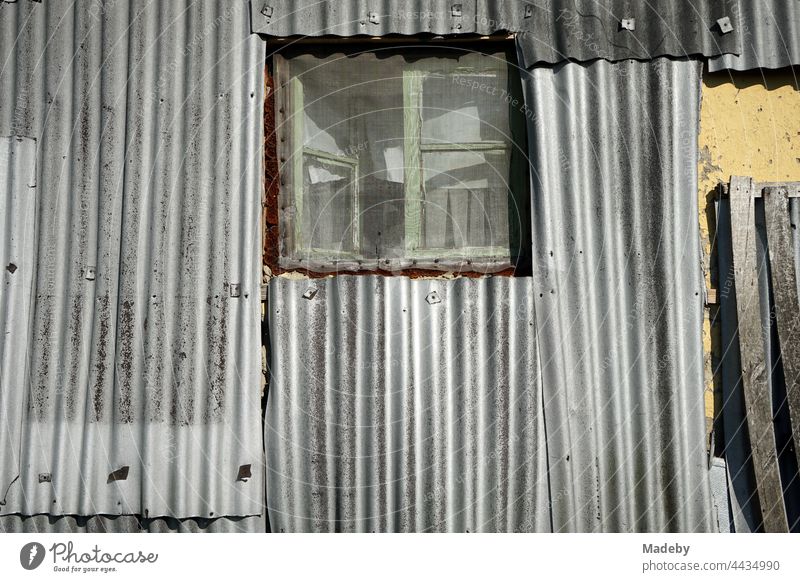 Old wooden window with insect screen in old silver-grey corrugated iron facade of a residential house in summer sunshine in the village of Maksudiye near Adapazari in the province of Sakarya in Turkey