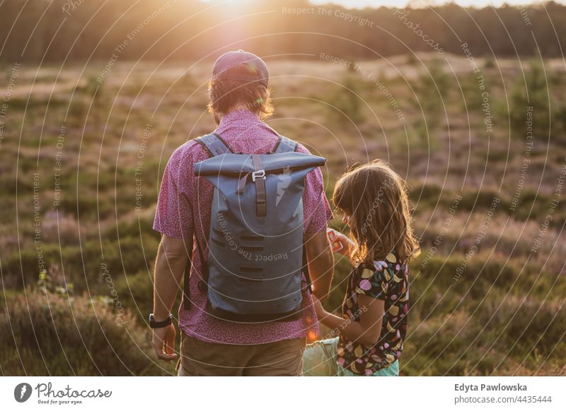 Father and daughter on a hike in the forest during sunset together father parent love back backpack walk meadow grass field rural countryside adventure