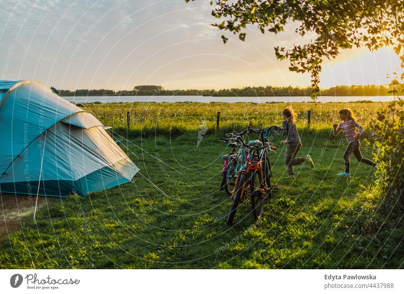 Children playing on the campsite running playful fun joy children family kids camping tent bike cycling meadow grass field rural green countryside adventure