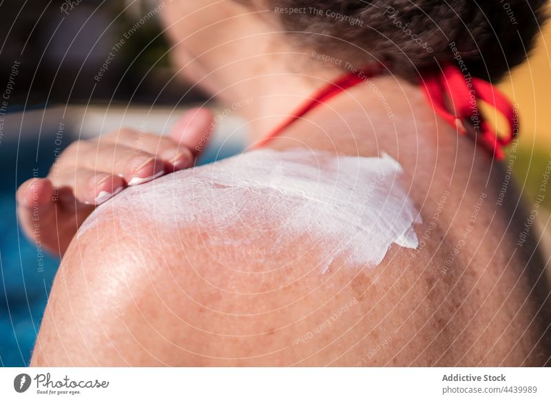 Anonymous old woman smearing lotion while relaxing on poolside senior sunbath sunblock cream apply positive hydrate chill female carefree water gray hair summer