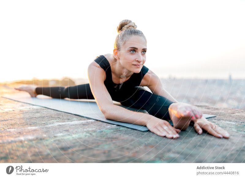 Flexible woman in Wide Splits pose on sports mat wide splits spirit yoga sundown posture rooftop stretch body care flexible female asana upavishta konasana