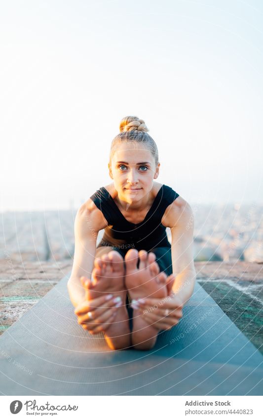 Smiling barefoot woman doing Seated Forward Bend seated forward bend yoga sunset posture healthy practice stretch wellbeing fit female paschimottanasana