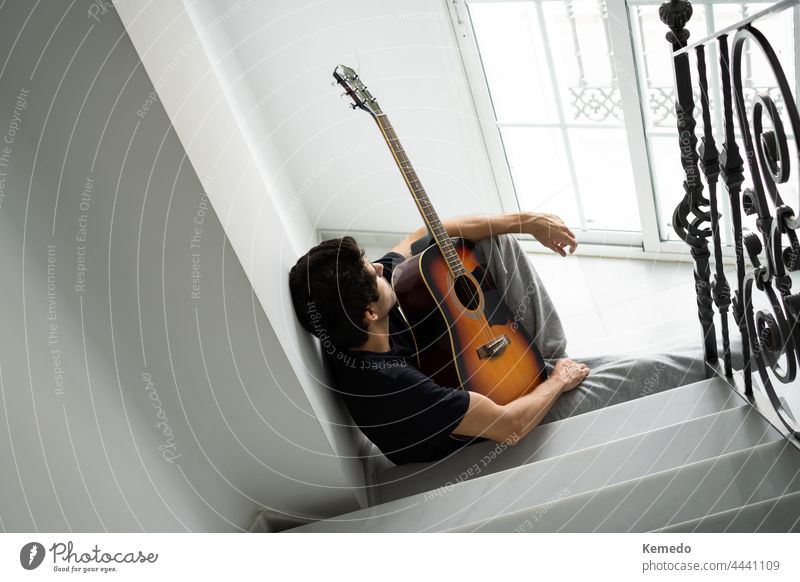 Thoughtful young man on staircase takes a break from playing guitar. music musician guitarist person inspiration idea uninspired unmotivated bored thoughtful