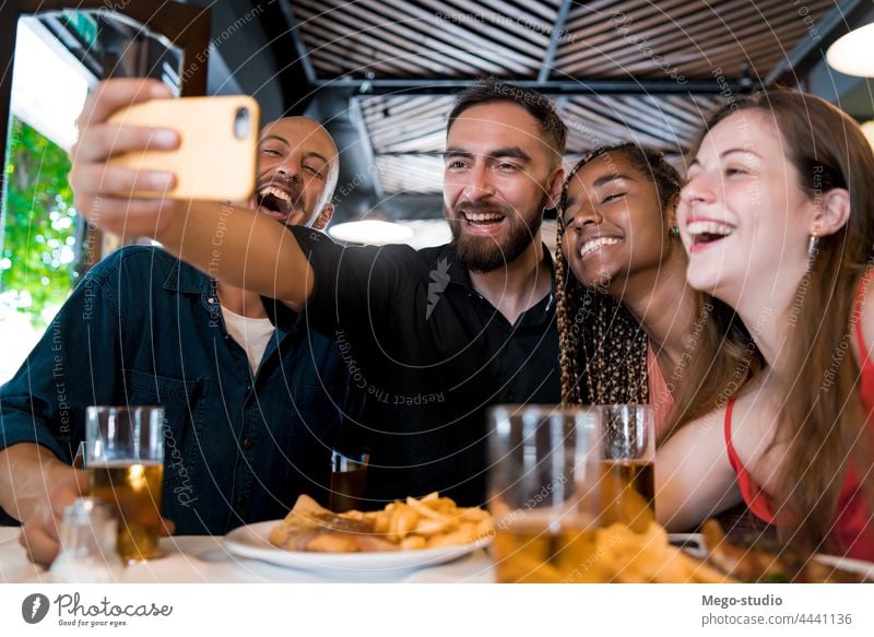 Group of friends taking a selfie with a mobile phone at a restaurant. together drink beer food meal friendship indoors enjoyment smartphone social media happy