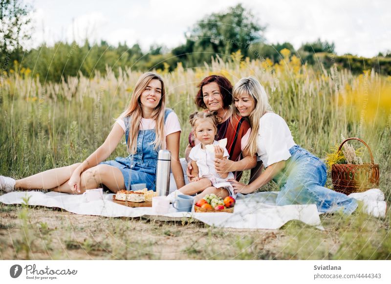 The family is having a picnic on the lawn. Three generations of women of the same family rest together woman mother grandmother daughter granddaughter summer