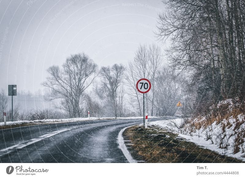 the curve of a country road in winter. In the foreground a traffic sign 70 Poland Winter Curve Street Snow Exterior shot Cold Deserted Tree Landscape Nature