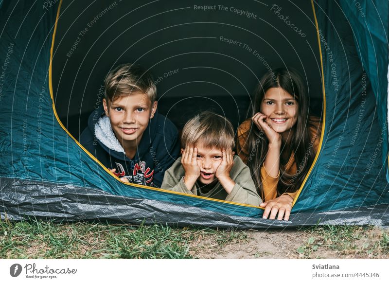 Smiling children lie together in a tent at a camping site. Family time, family vacation, hiking on the weekend smiling girl boy lifestyle leisure
