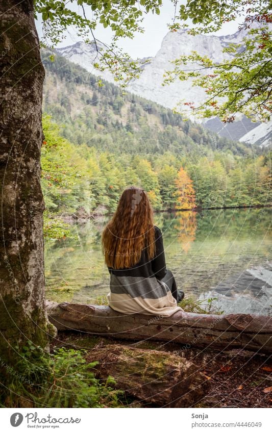 Young woman with long red hair sits by a lake and enjoys the view Woman youthful Lakeside Sit Tree trunk Forest Autumn Rear view long hairs Red lured pretty