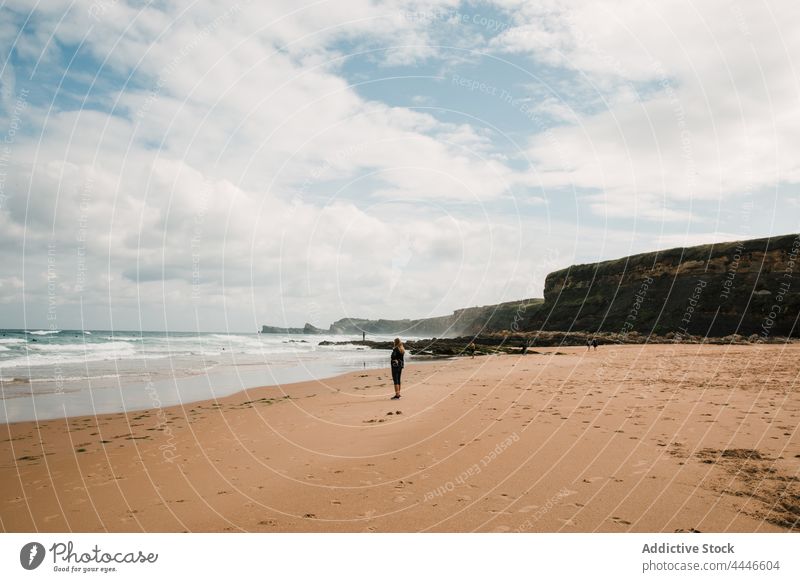 Woman standing near waving sea on beach woman wave tourist summer vacation cliff blue sky cloudy spain female coast shore resort holiday ocean sand water rest