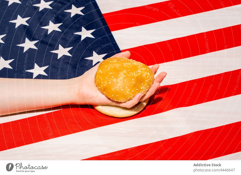 Crop person with cut bun on American flag hamburger fast food usa national holiday celebrate concept independence day democracy patriotism baked sesame seed