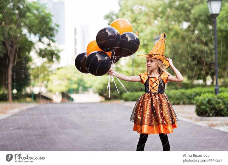 Little Caucasian Girl in costume of which holding hand hot air balloons orange and black color and celebrating Halloween halloween witch hat child girl