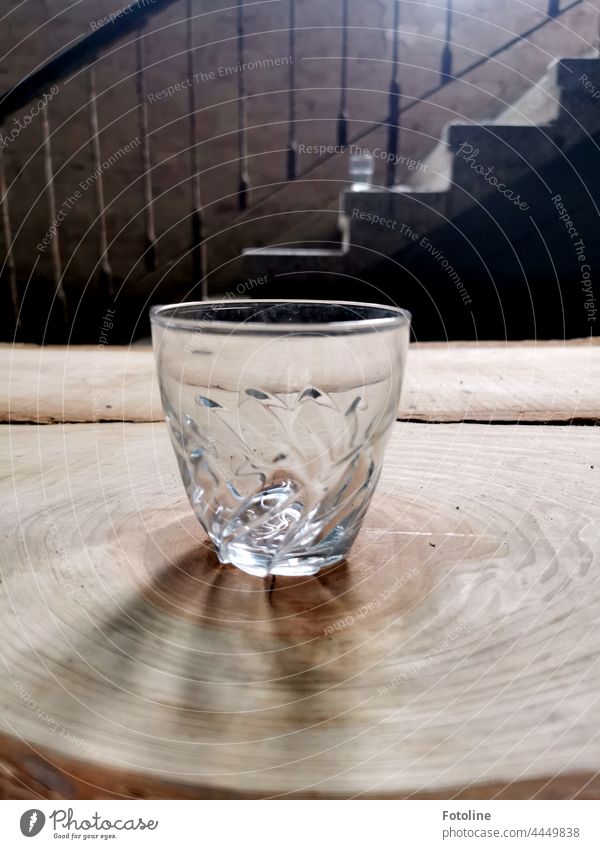 On a tree slice in front of an old staircase in a Lost Place stands an empty glass. Glass drinking glass Juice glass Tree section Wood grain Stairs Banister