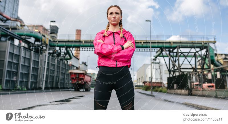 Sportswoman with crossed arms posing in front of a factory sportswoman self-confident looking straight ahead serious runner banner web header panorama panoramic