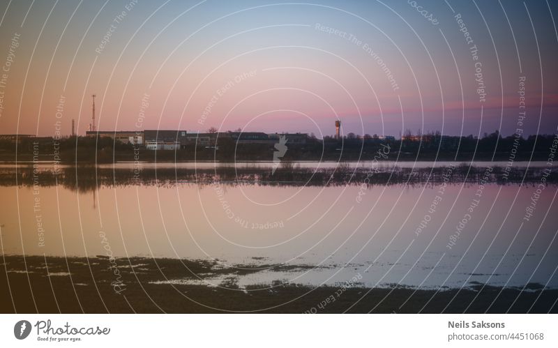 calm waveless flood water on meadow in Latvia, beautiful spring evening sunset, clear sky, factory in distance abstract afternoon background beauty black blue