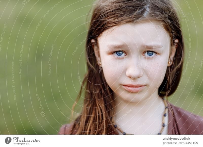 Portrait of sad crying emotional cute little girl looking at camera with face of deep sadness and sorrow outdoors. Sad child with blue eyes, copy space portrait