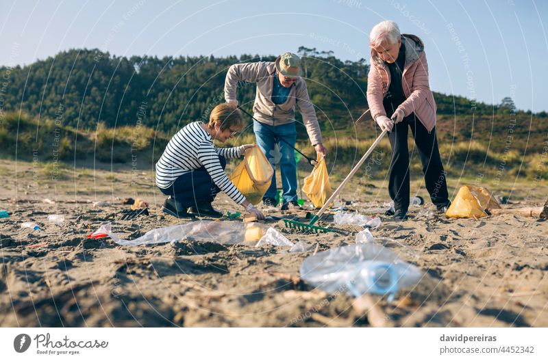 Senior volunteers cleaning the beach senior group picking up trash rake picking up clip crouched dirty volunteering ecological conscience tools family