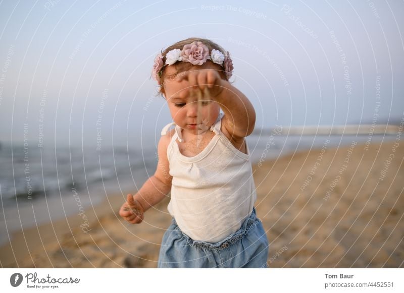 Girl with flowers in her hair plays with sand on the beach - time trickles through her fingers Baby Toddler Child Hand Face Fingers 0 - 12 months Eyes Looking