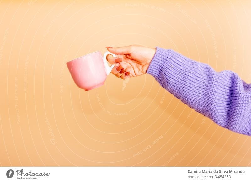 Closeup of female hands holding a light pink cup. Girl with beautiful nails. holding cup of tea or coffee. Studio photo. Photo for cropping. Empty. autumn