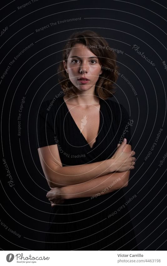 A young beautiful woman looking at the camera in a studio shot in black dress and background 20-25 adult attractive casual close-up concepts confident dark
