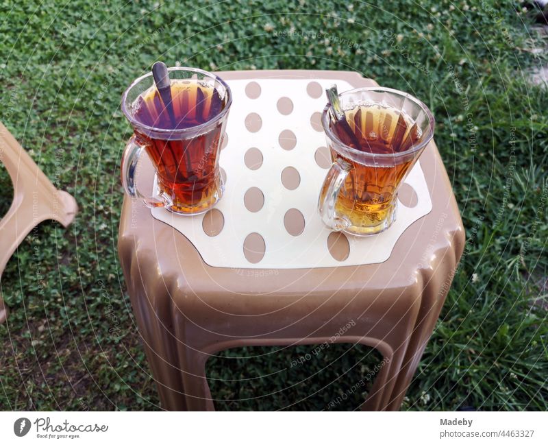 Turkish tea glasses with teaspoons and tea on a plastic stool in brown and beige on a green lawn in a garden in the village of Maksudiye in Sakarya province, Turkey