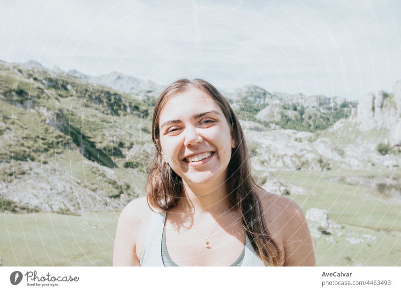 Portrait of young smiling woman face partially covered with flying hair in windy day standing at mountain - carefree woman enjoyment freedom horizontal person