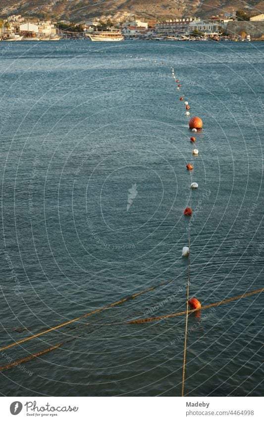 Floats and buoys mark the swimming area at the harbour at the bay of Foca in summer in the light of the evening sun at the Aegean Sea in the province of Izmir in Turkey.