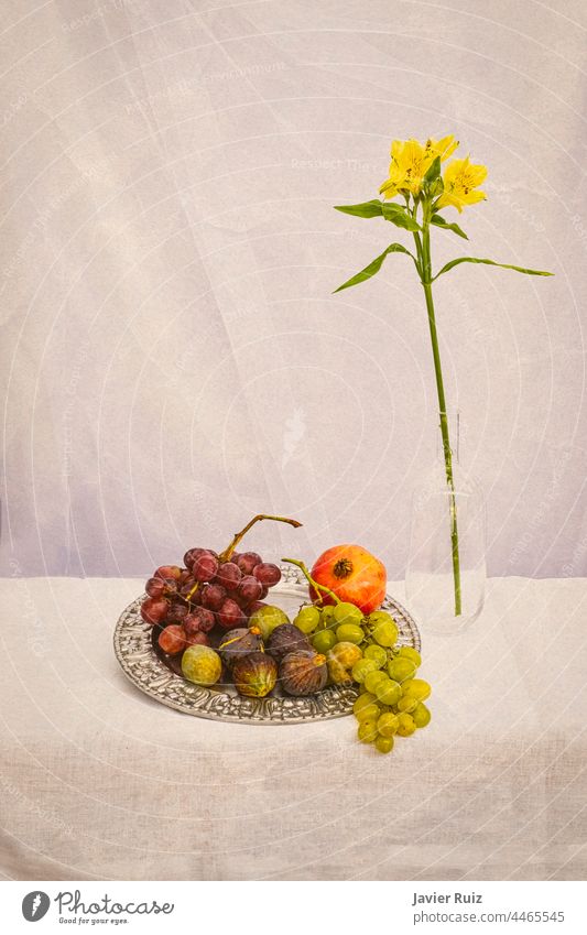 still life of flowers and fruits on an earth colored background, with grapes, figs, a pomegranate on a silver plate and a yellow flower a glass jar still live