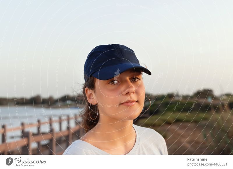 Teen girl in dark blue baseball cap standing by the sea at sunset. Cap mockup outdoor teenager adolescent Caucasian visor wearing t-shirts teen girl childhood