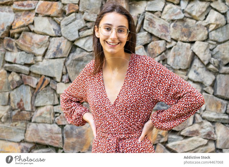Positive female standing with hands on waist against stone wall woman laugh happy cheerful smile glad brunette positive young style dress joy fun content